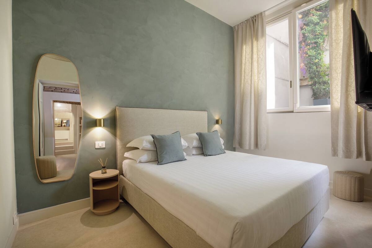 A neatly arranged bedroom with a large bed, bedside lamps, a round bedside table, and a mirror.