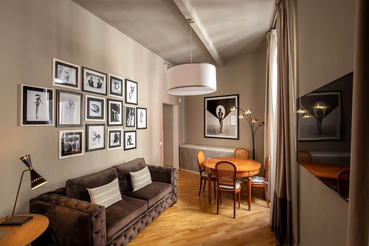 A modern living room with a brown sofa, a dining table with chairs, and a large white pendant light.