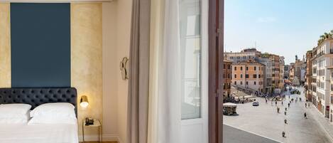A hotel room with a large bed, a bedside table with a lamp, and a view of a busy street with historic buildings.