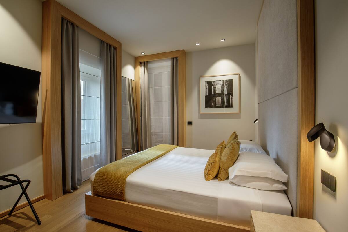 A modern hotel room with a large bed, wooden headboard, and a flat-screen TV mounted on the wall.
