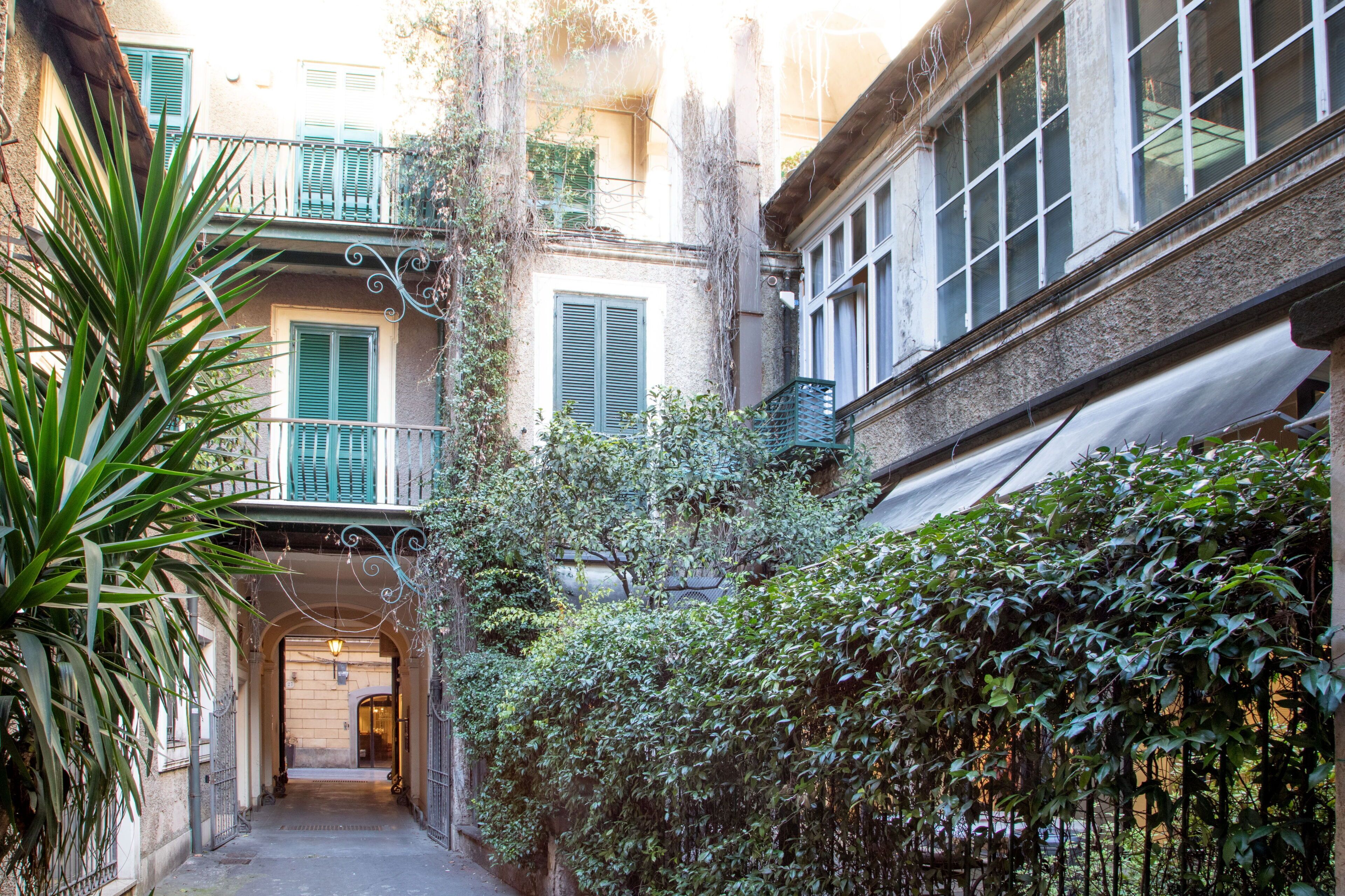 Une ruelle étroite, avec un immeuble sur la droite, doté d’un balcon aux volets verts et d ’une fenêtre avec un store blanc.