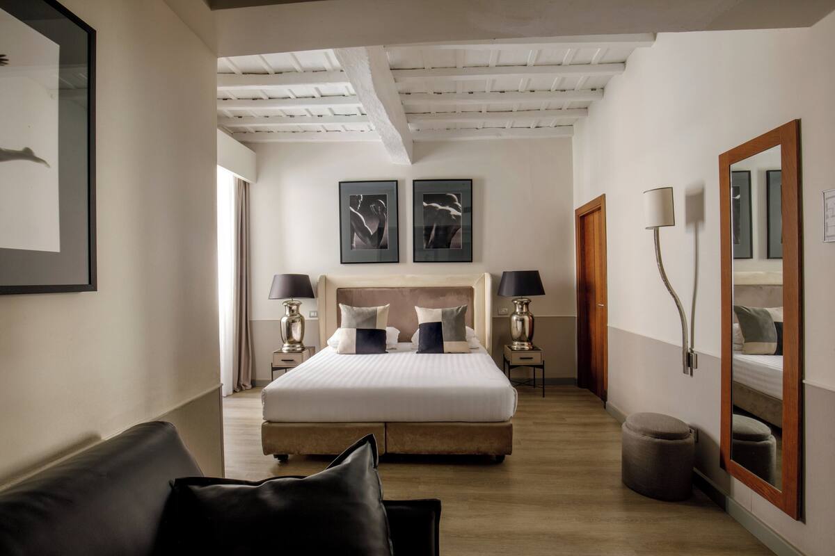 A modern hotel room with a large bed, bedside tables, a mirror, and artwork on the walls.