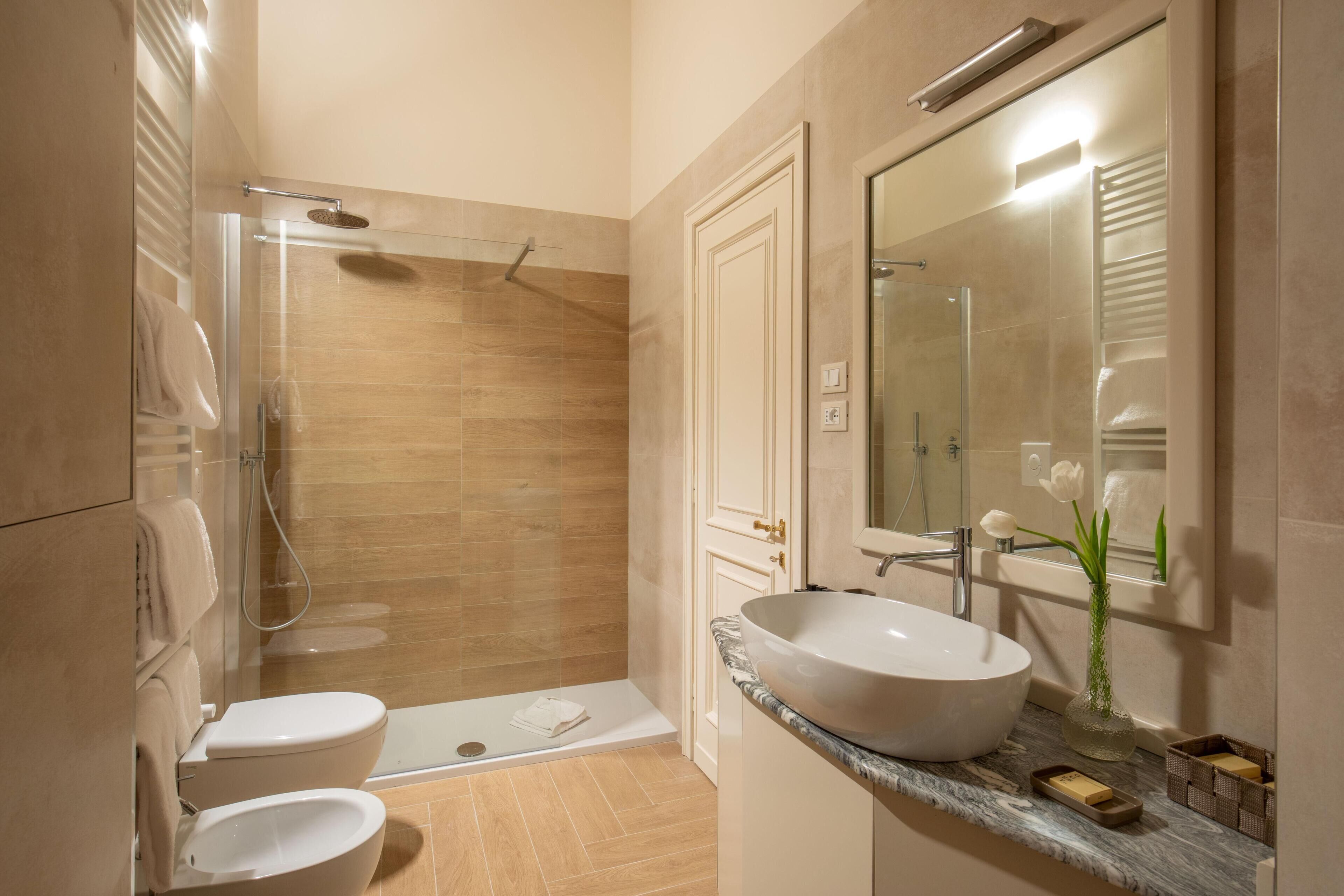 Un baño moderno con ducha de vidrio, lavamanos blanco y un espejo grande.