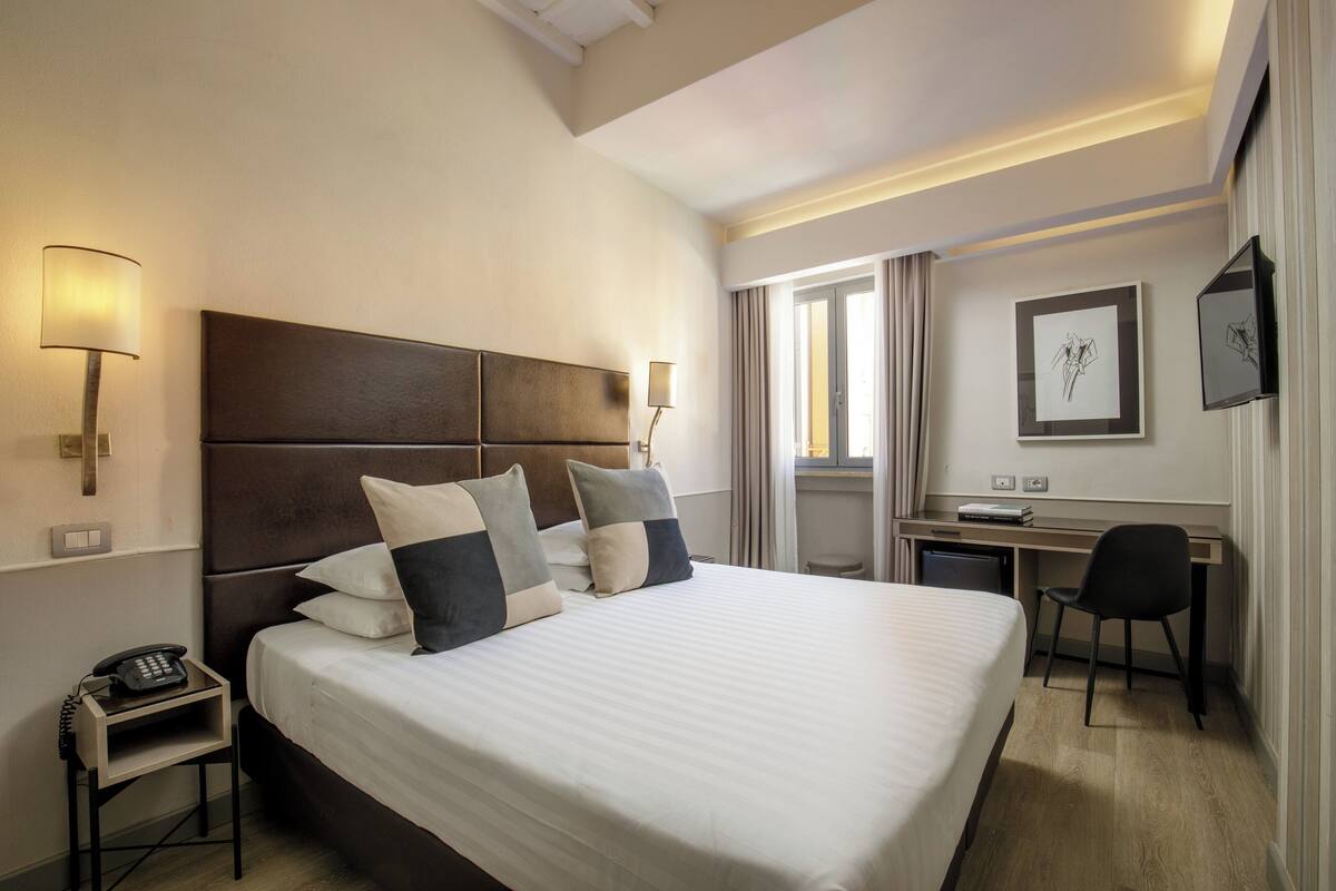 A hotel room with a large bed, bedside lamps, a desk, and a chair.