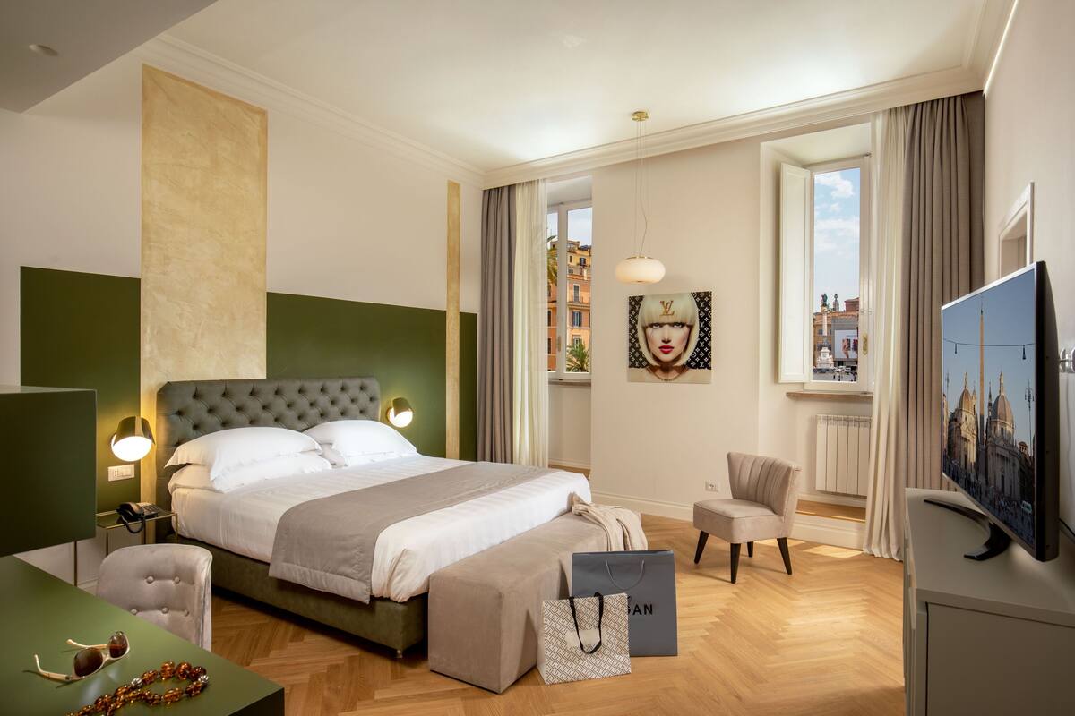 A modern hotel room with a large bed, a desk, a chair, a TV, and a view of the city.