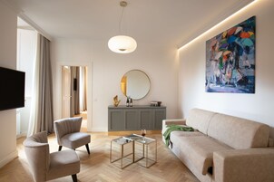 A modern living room with a sofa, two armchairs, a coffee table, a flat-screen TV, a large painting, and a mirror on the wall.