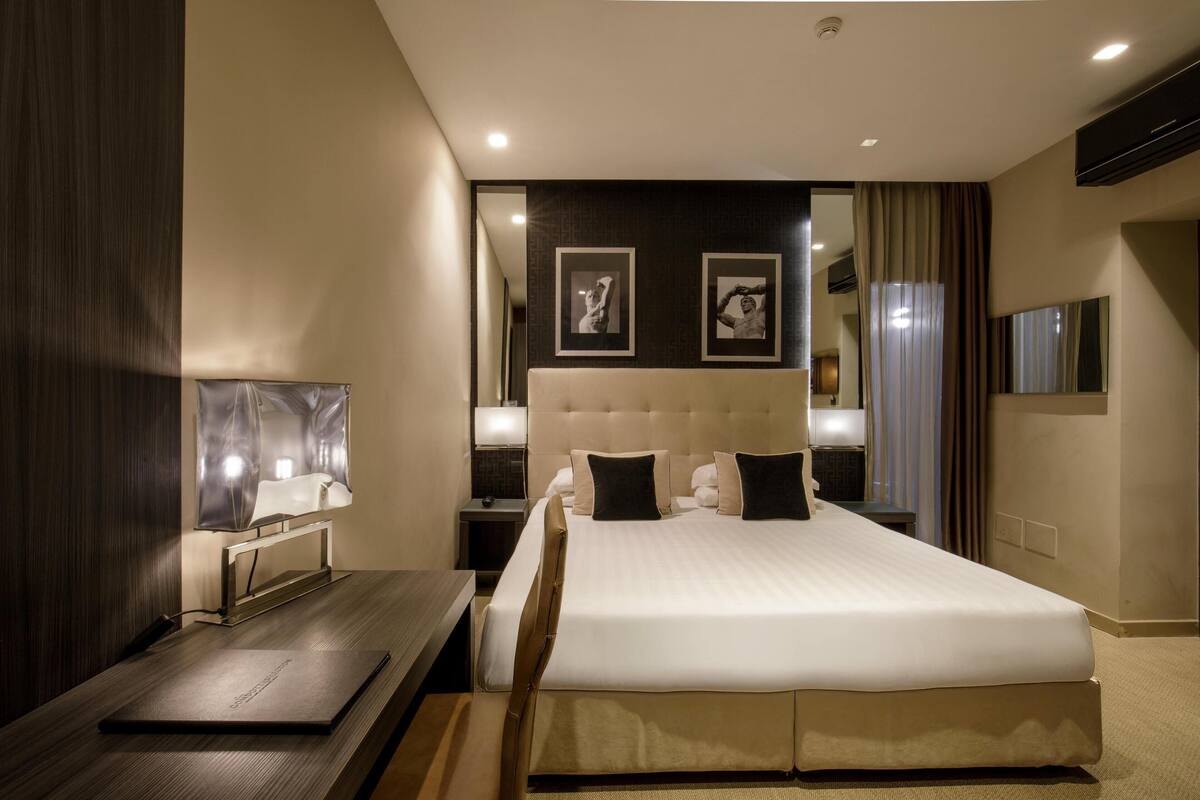 A modern hotel room with a large bed, a desk, a mirror, and a TV.