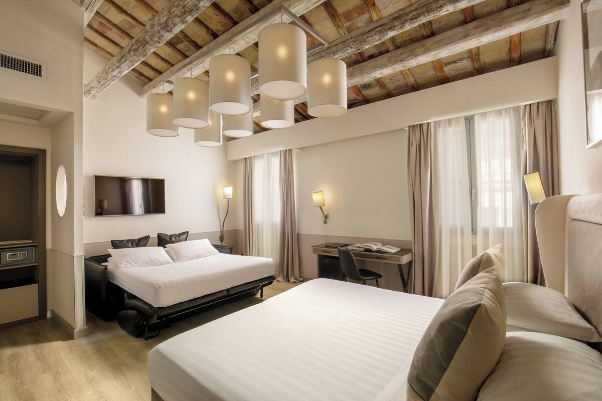 A hotel room with a large bed, a desk, a chair, and a TV mounted on the wall.