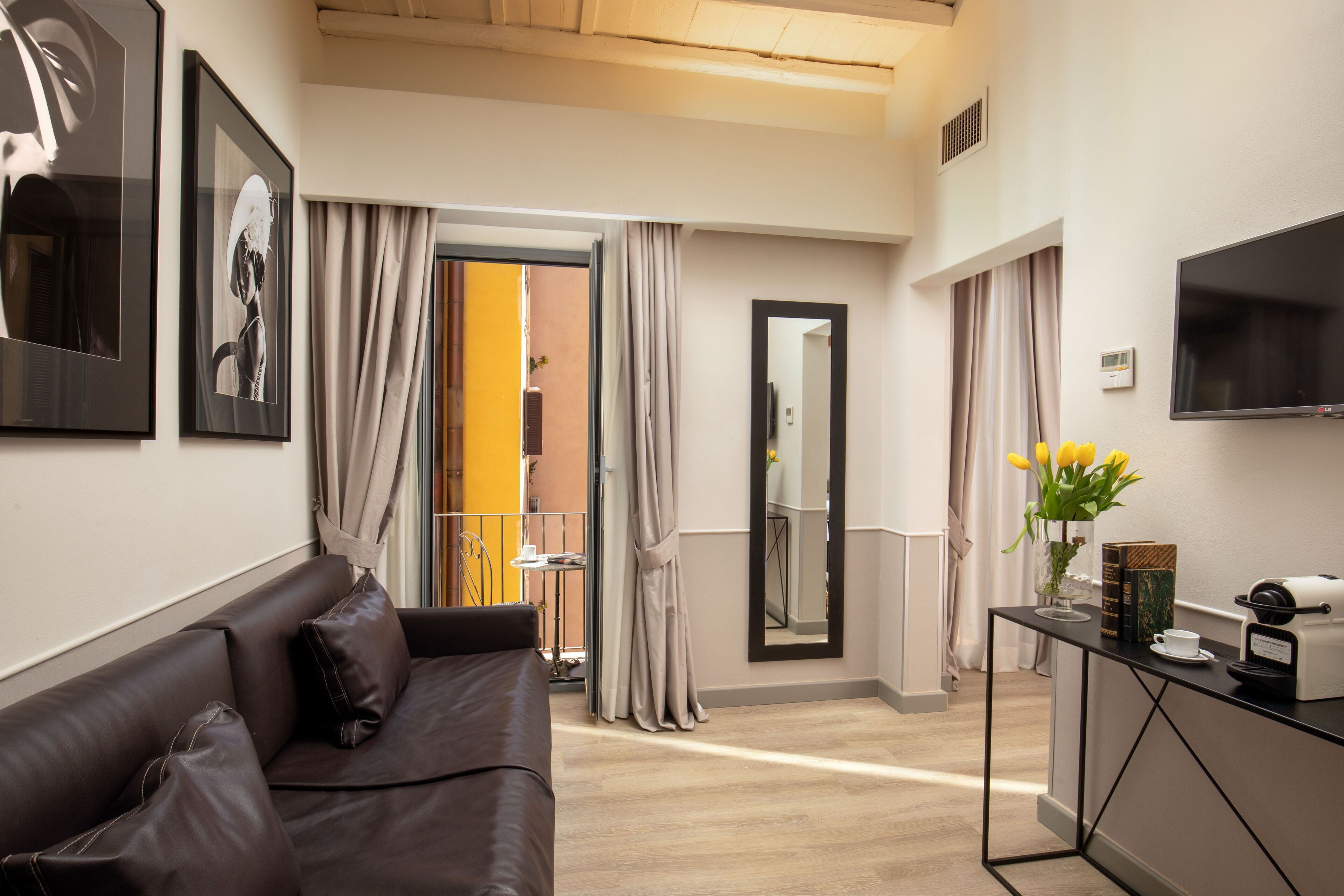 A modern hotel room with a leather sofa, a coffee machine, a flat-screen TV, and a large mirror.