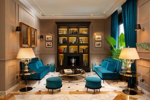 A luxurious living room with a blue sofa set, a coffee table, and a bookshelf filled with books and decorative items.