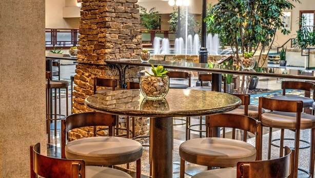 A restaurant with round tables and chairs, a stone pillar, and a fountain in the background. - Radisson Hotel Fort Worth North-Fossil Creek (Fort Worth)