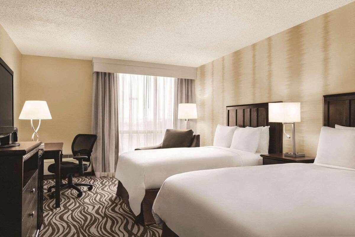 A hotel room with two beds, a desk with a chair, a television, and lamps.