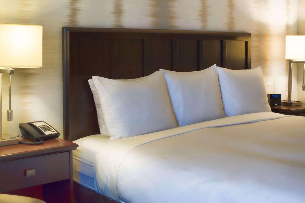 A hotel room with a large bed, a bedside telephone, and a nightstand with a lamp.