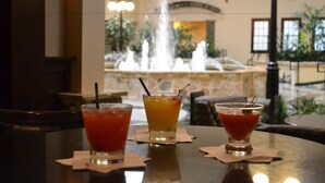 A bar area with three drinks on a table, a fountain in the background, and a stone wall. - Radisson Hotel Fort Worth North-Fossil Creek (Fort Worth)