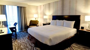 A hotel room with a large bed, two bedside tables with lamps, a desk with a chair, and a large window with curtains. - Radisson Hotel Fort Worth North-Fossil Creek (Fort Worth)