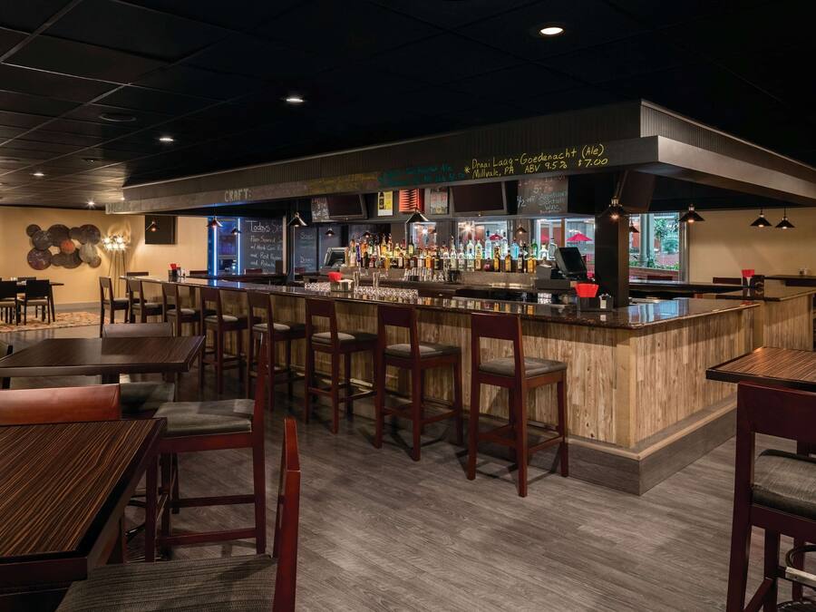 A bar area with wooden bar stools, a counter with various bottles, and a menu board.