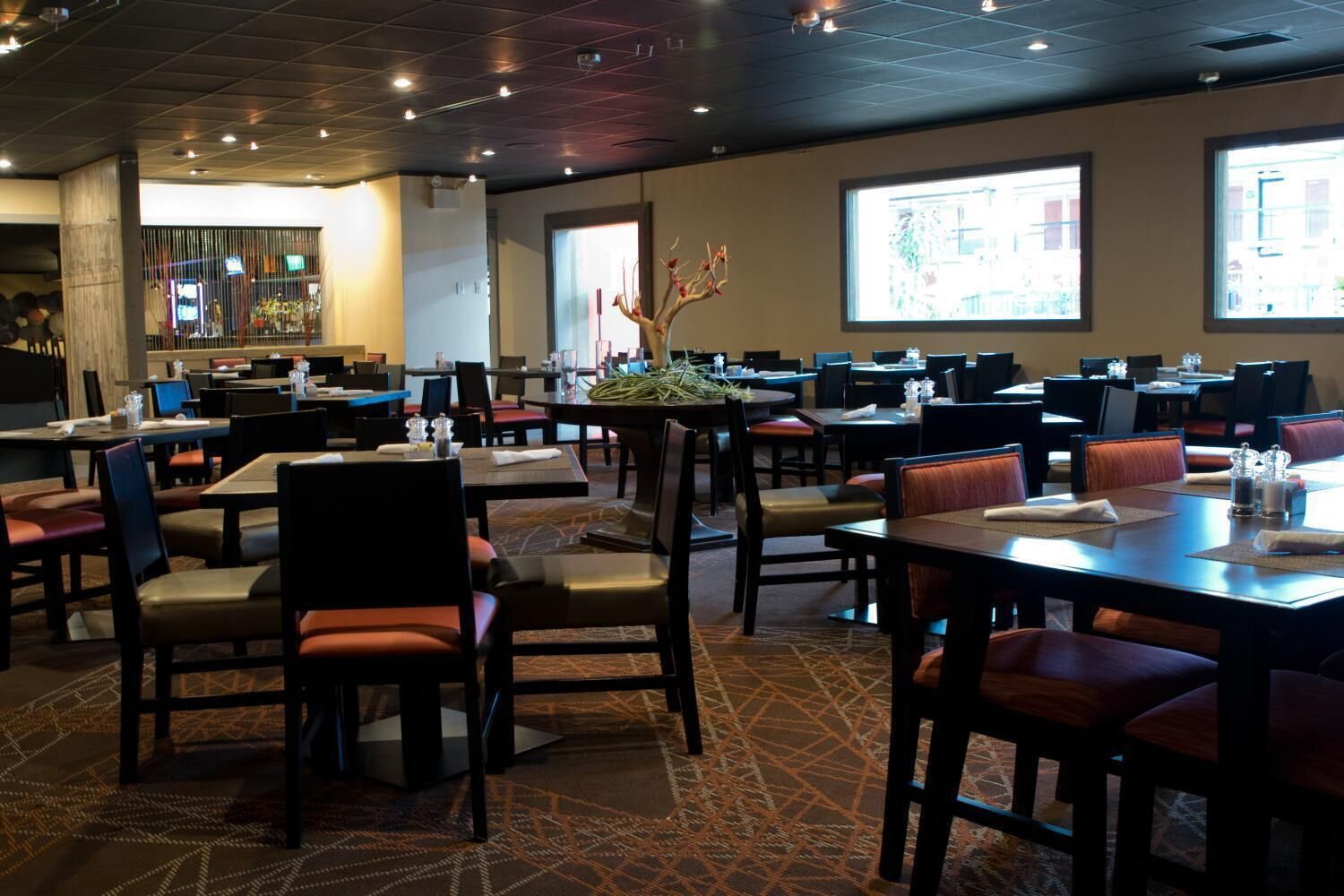 A restaurant with multiple tables and chairs, a patterned carpet, and a large window with a view.