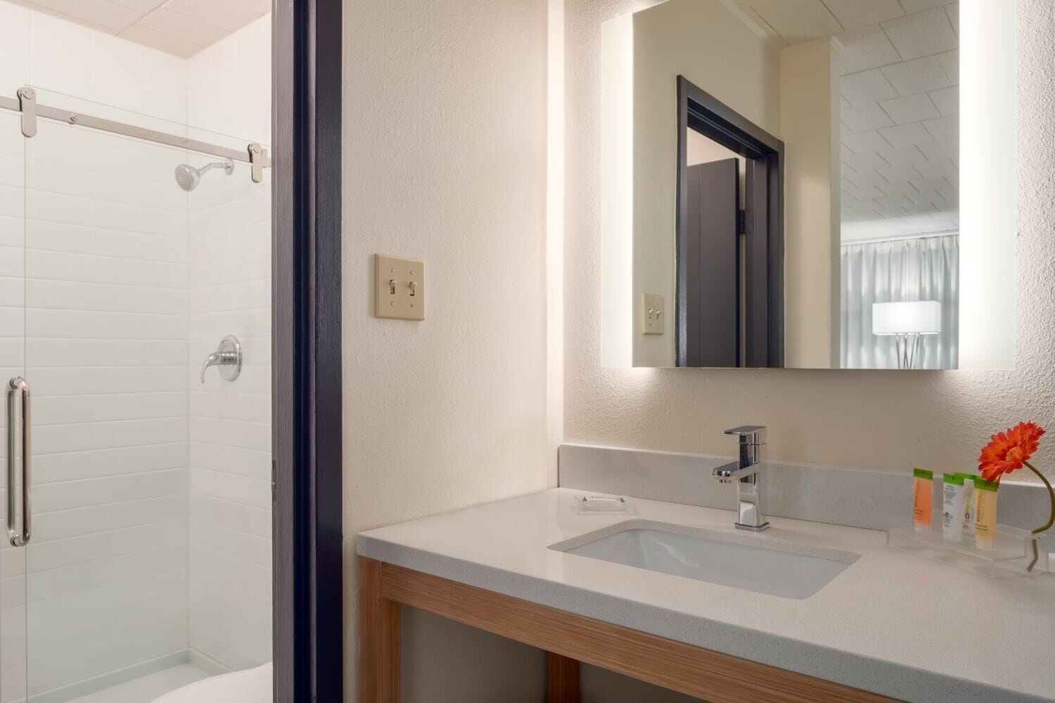 A bathroom with a shower, a sink, a mirror, and a wooden cabinet.