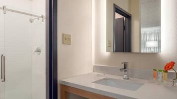 A bathroom with a shower, a sink, a mirror, and a wooden cabinet.