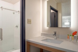 Een badkamer met een douche, een wastafel, een spiegel en een houten kastje.