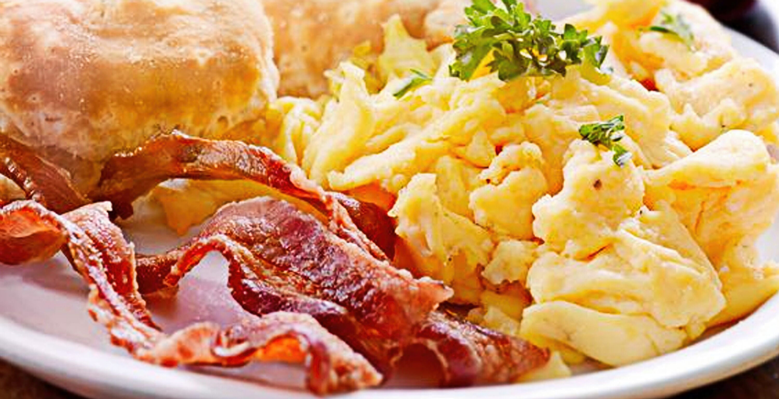 Une assiette avec des œufs brouillés, du bacon et un biscuit.