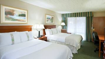 A hotel room with two beds, a desk, a chair, a lamp, and two paintings on the wall.