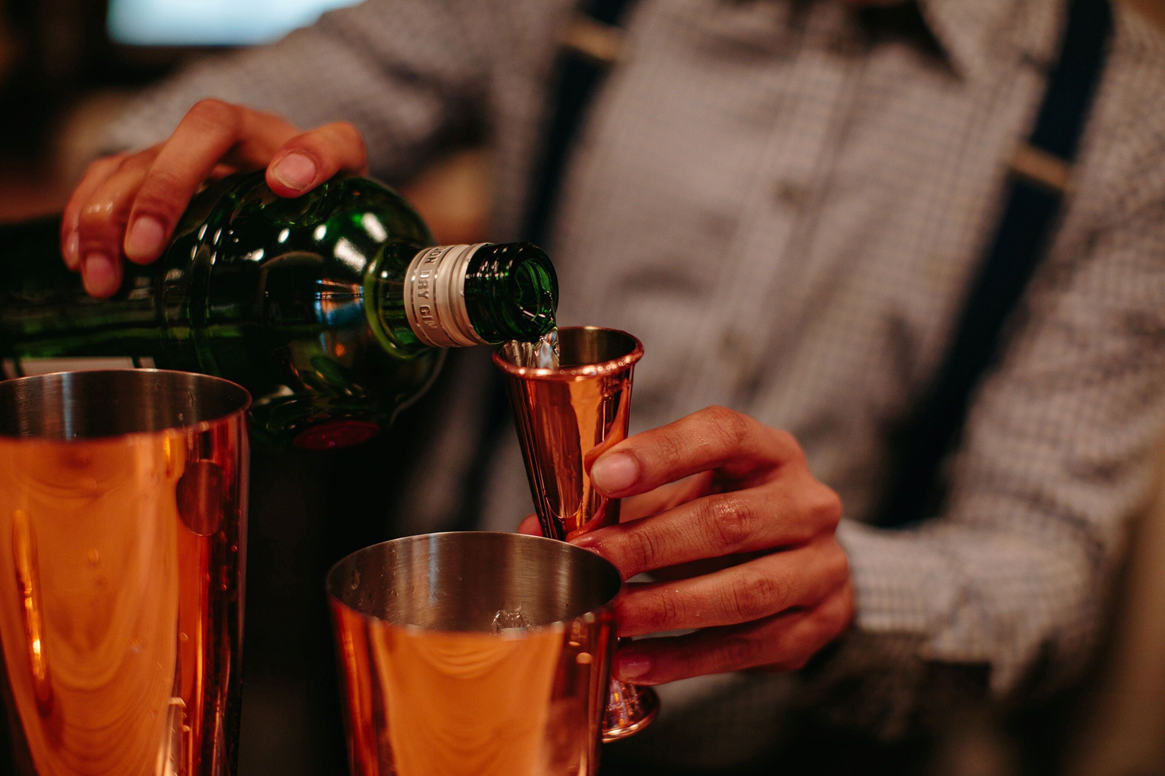 Iemand giet een vloeistof uit een groene fles in een koperen beker.