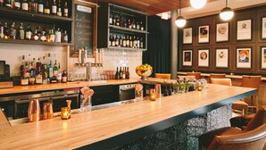 A bar area with shelves of liquor bottles, a chalkboard menu, and framed pictures on the wall.