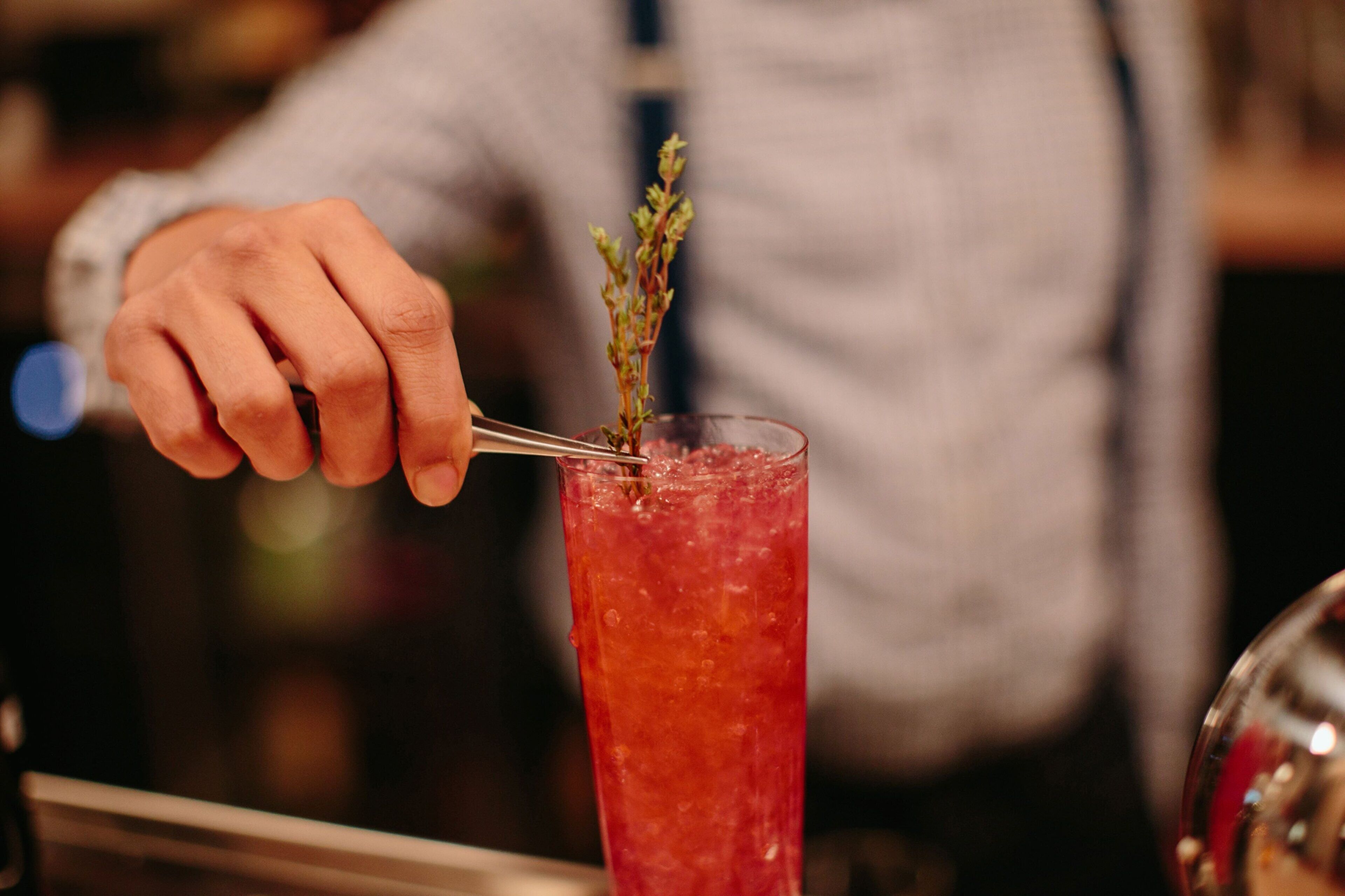 A bartender garnishing a tall glass with a sprig of herb.