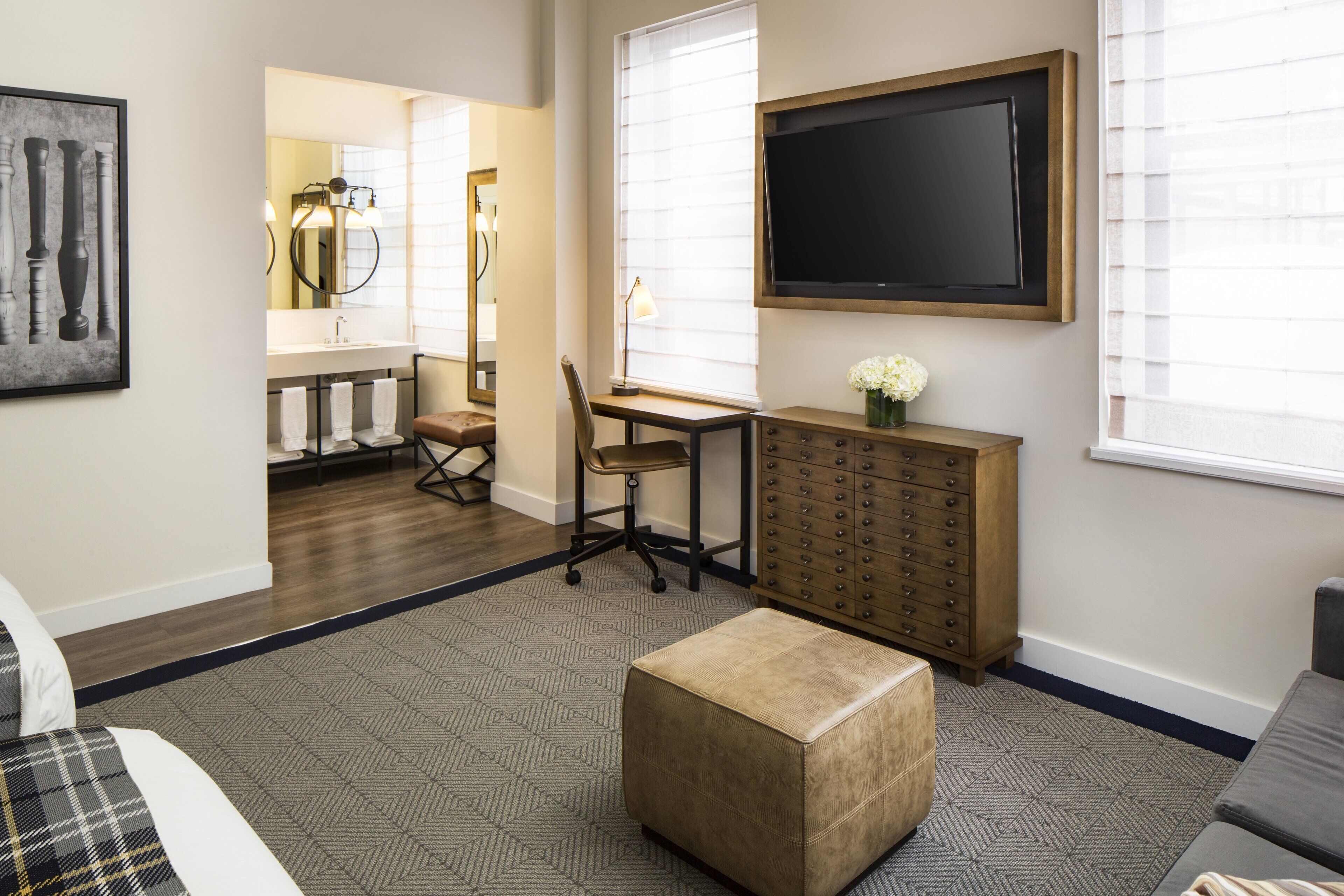 A hotel room with a bed, a desk, a chair, a dresser, and a large window.