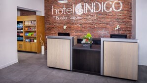 A hotel reception desk with a brick wall backdrop, a wooden cabinet with a plant, and a sign reading "hotel INDIGO at Boston Garden".