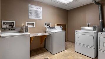 A guest laundry area with washing machines and dryers, a sign with laundry instructions, and a vent pipe on the ceiling.