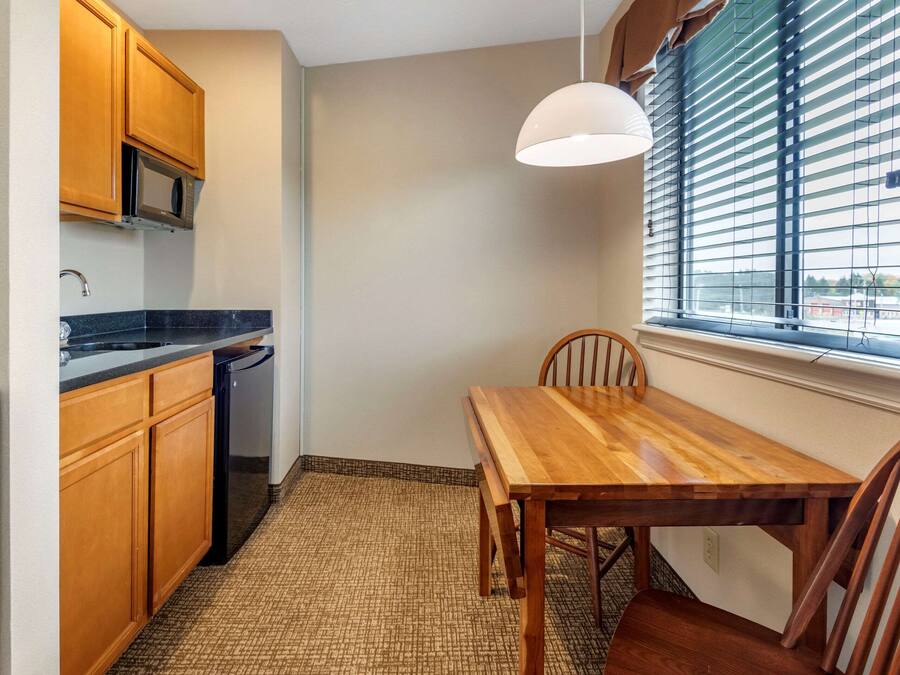 A compact kitchen with wooden cabinets, a microwave, a sink, and a dining table with chairs.