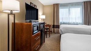 Une chambre d’hôtel équipée d’un téléviseur à écran plat, d’un bureau en bois, de deux lits, d’une lampe et d’une fenêtre avec des rideaux.