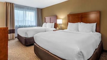 A hotel room with two beds, a wooden headboard, a bedside table with a lamp, and a large window with curtains.