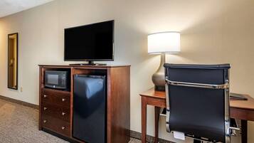 A hotel room with a flat-screen TV, a microwave, a mini-fridge, a desk with a lamp, and a black office chair.