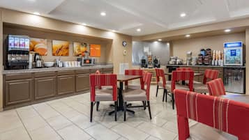 Un espace repas d’hôtel avec des banquettes rouges, un distributeur de café et un buffet.