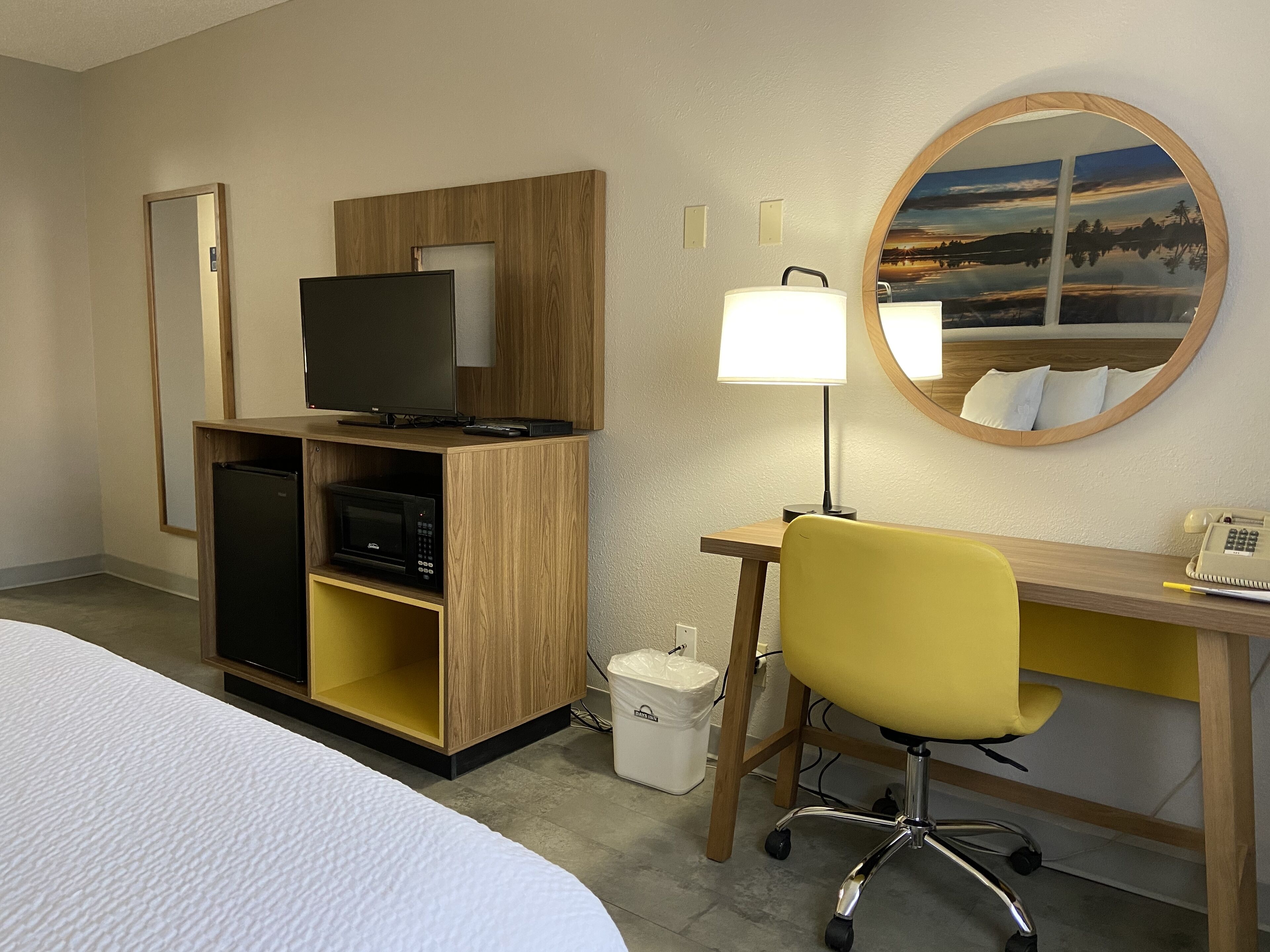 Une chambre d’hôtel comprenant un lit, un bureau avec une chaise, une télévision, une lampe, un téléphone et une petite poubelle.