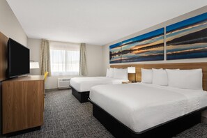 A hotel room with two beds, a TV, a desk, and a large painting of a sunset.