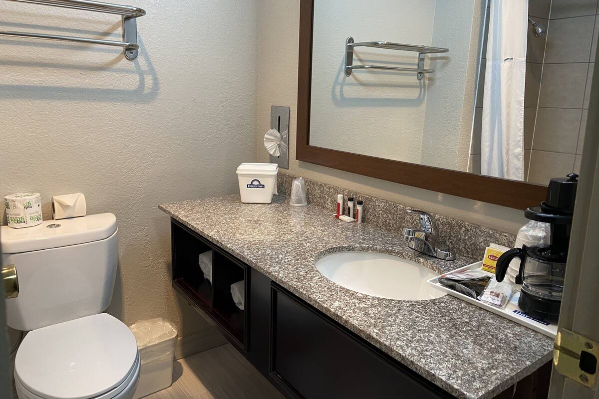 A bathroom with a white toilet, a granite countertop sink, a mirror, and a towel rack.