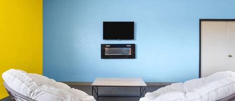 A room with two white cushioned chairs, a small table, a flat-screen TV, and a framed picture on the wall.