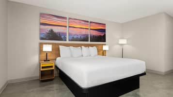 A modern hotel room with a large bed, two bedside tables, and a wall-mounted artwork depicting a sunset.