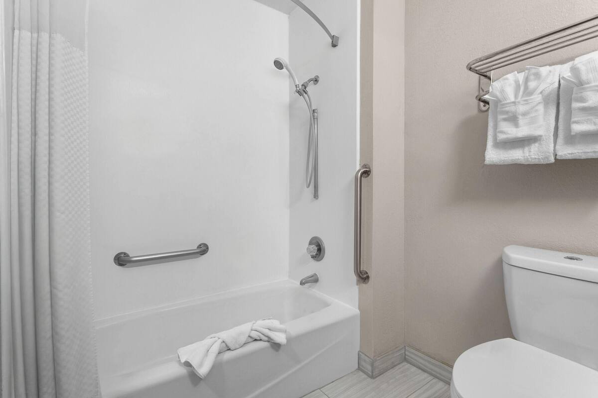 A bathroom with a bathtub, shower, and toilet. There are towels hanging on a rack.