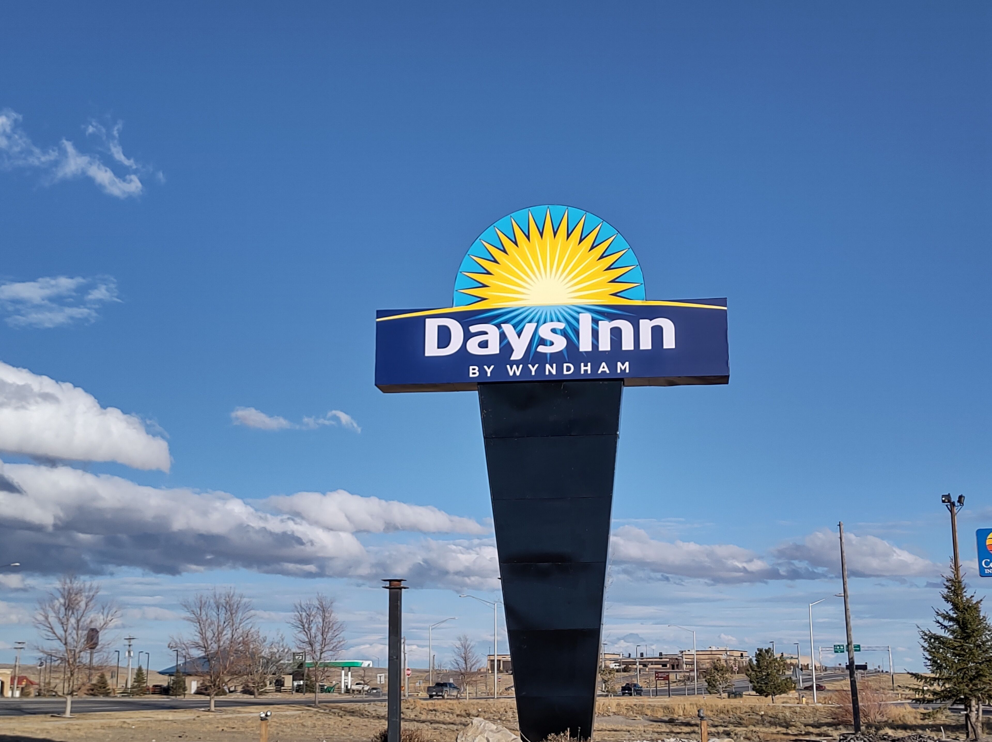 A Days Inn sign with a sunburst logo and the text "Days Inn by Wyndham" against a clear blue sky.