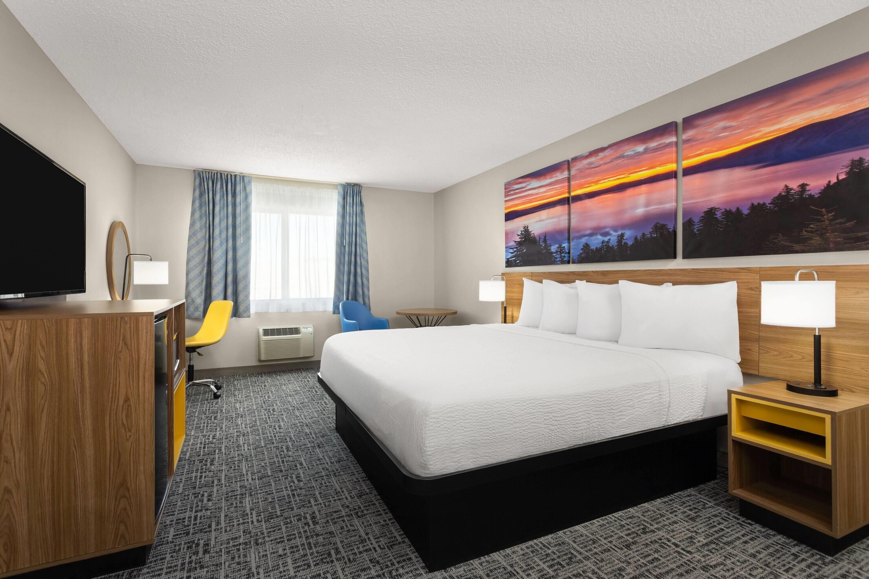 A hotel room with a large bed, a desk, a chair, and a TV.