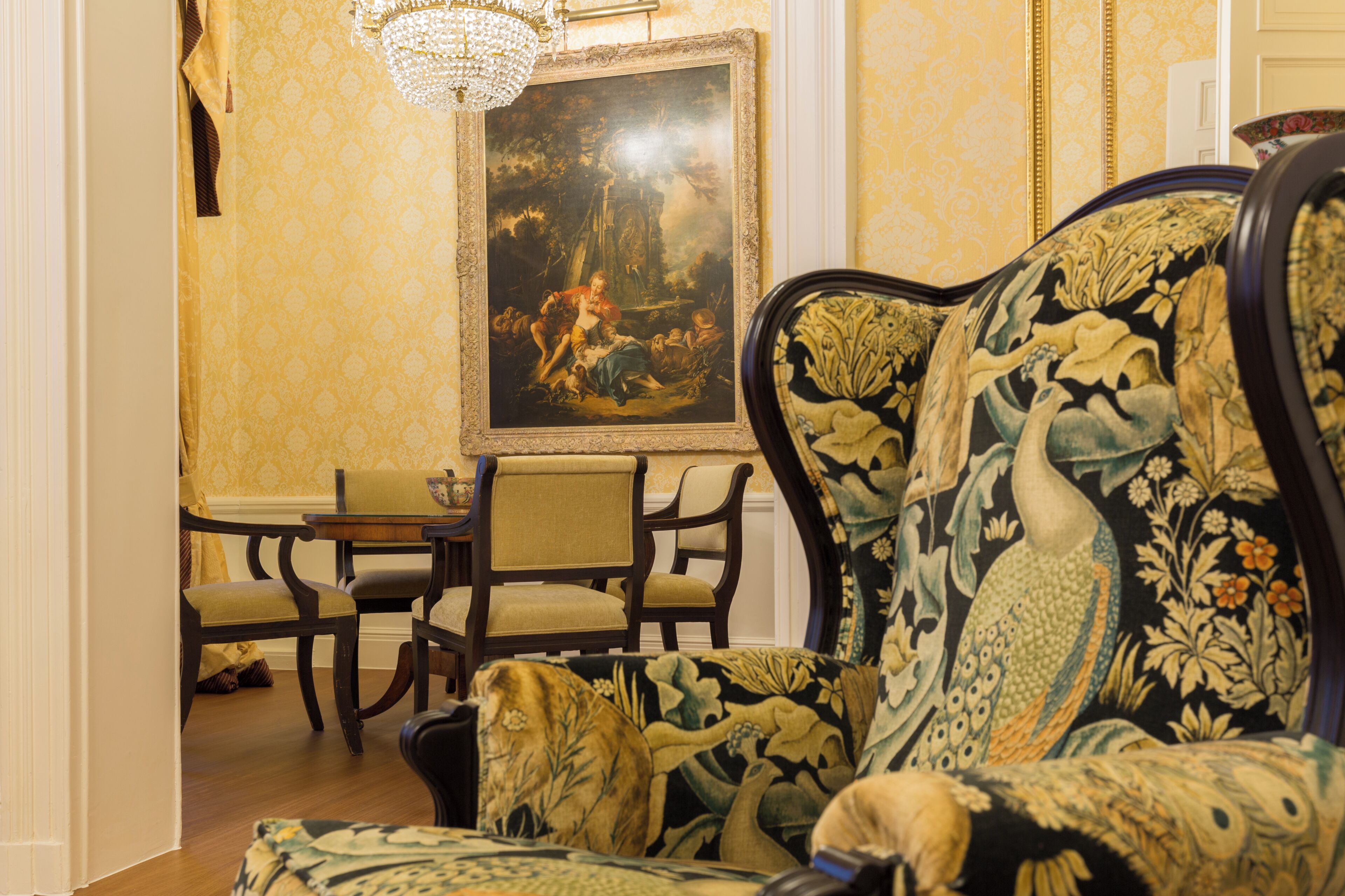 A room with a patterned sofa, a dining table with chairs, and a large framed painting on the wall.