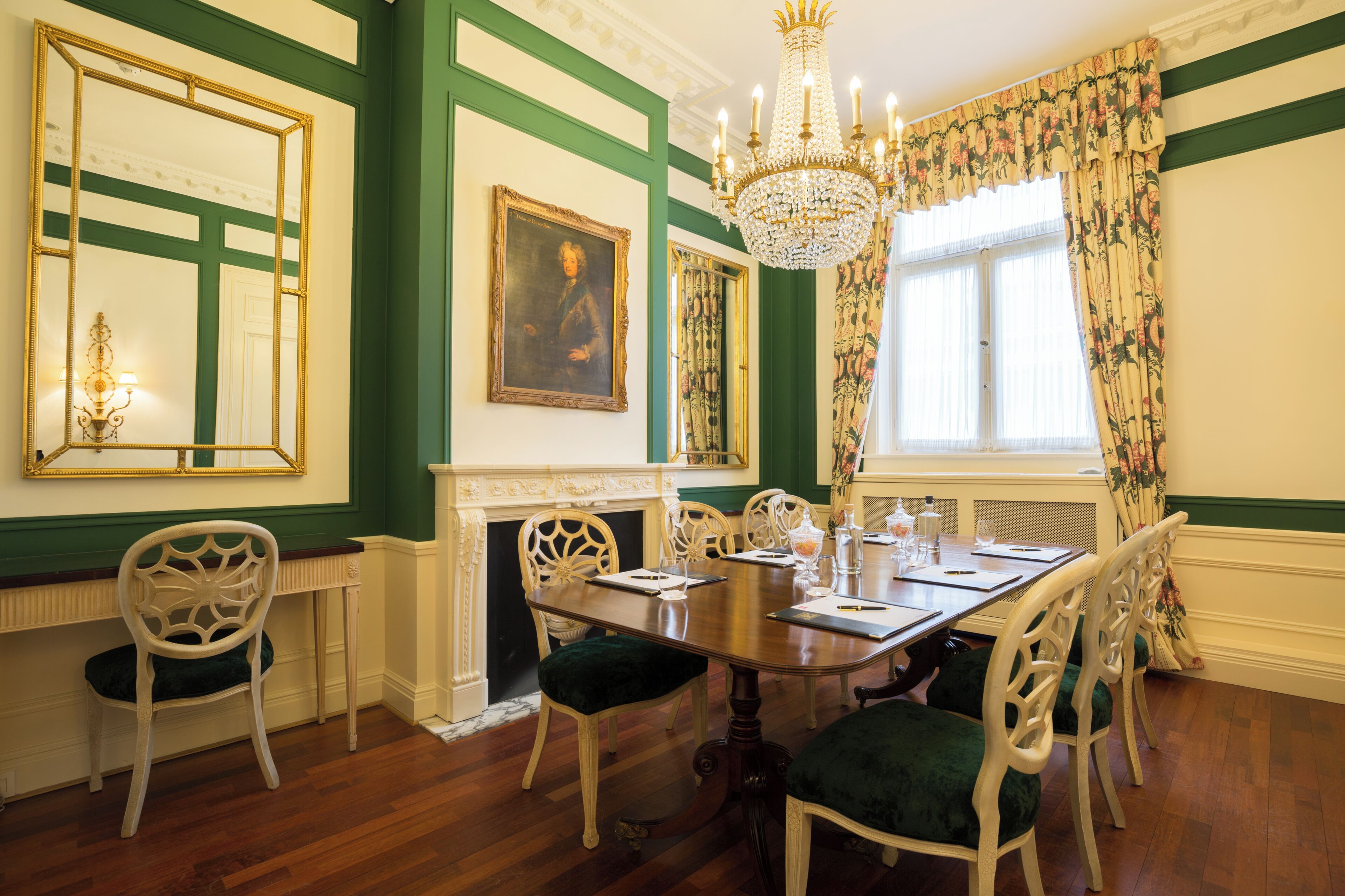 A dining room with a wooden table, white chairs, a chandelier, and green walls.