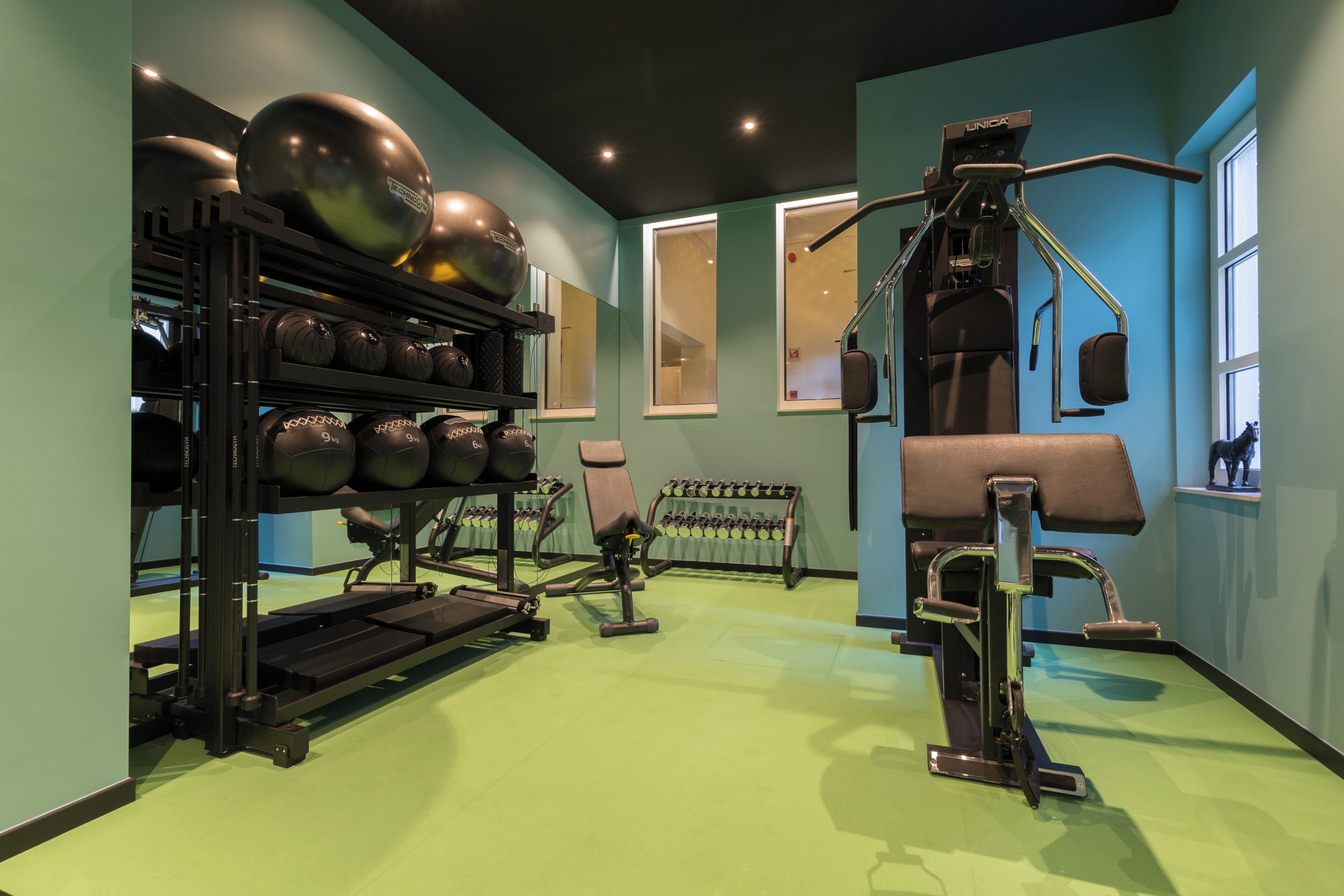 Een sportschool met trainingsapparatuur, een loopband en een wandrek met gewichten.