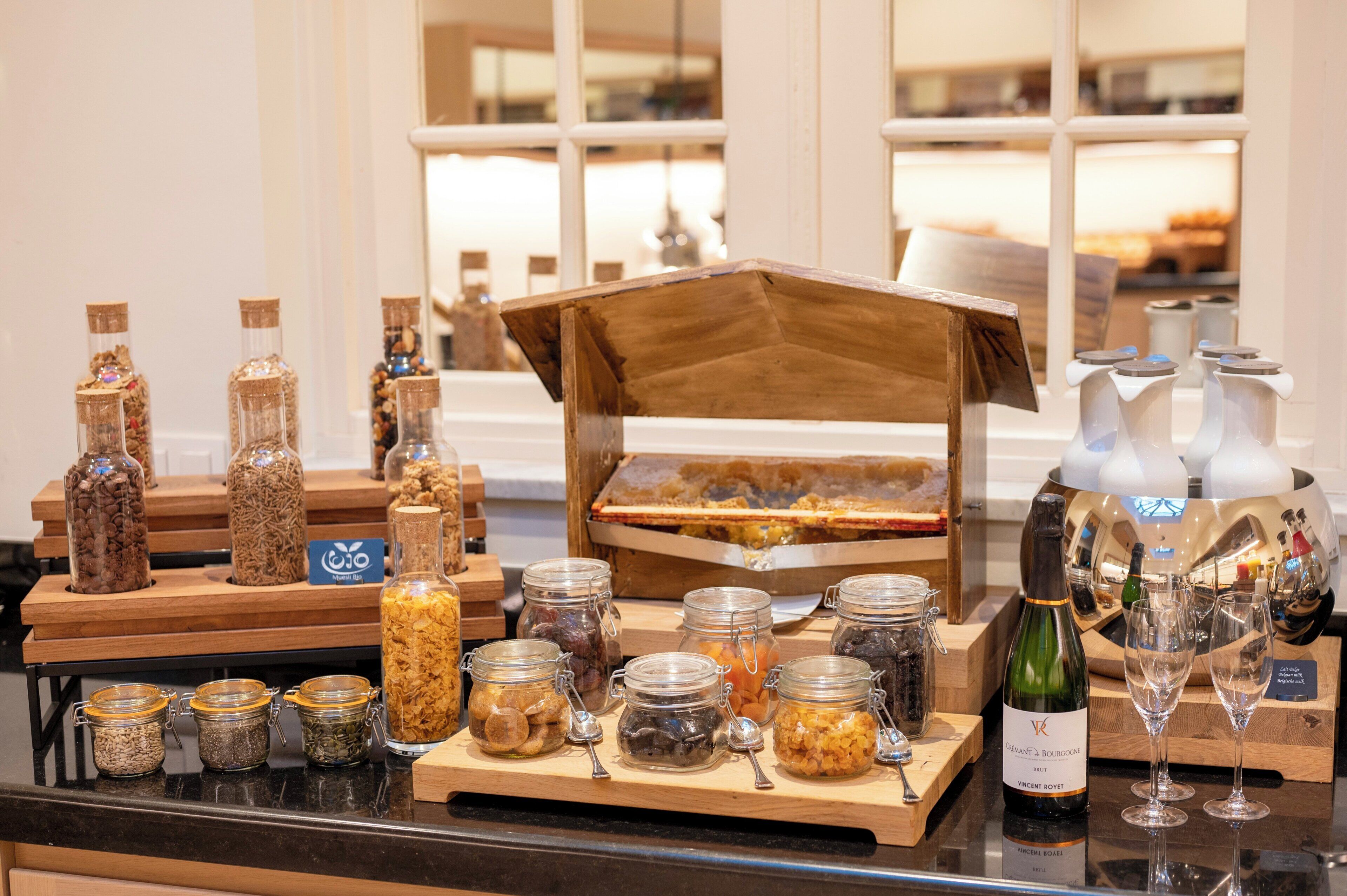 A buffet setup with various food items and beverages, including jars of pickles and a bottle of wine.