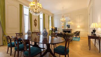 A formal dining room with a round table, chairs, chandeliers, and a television.